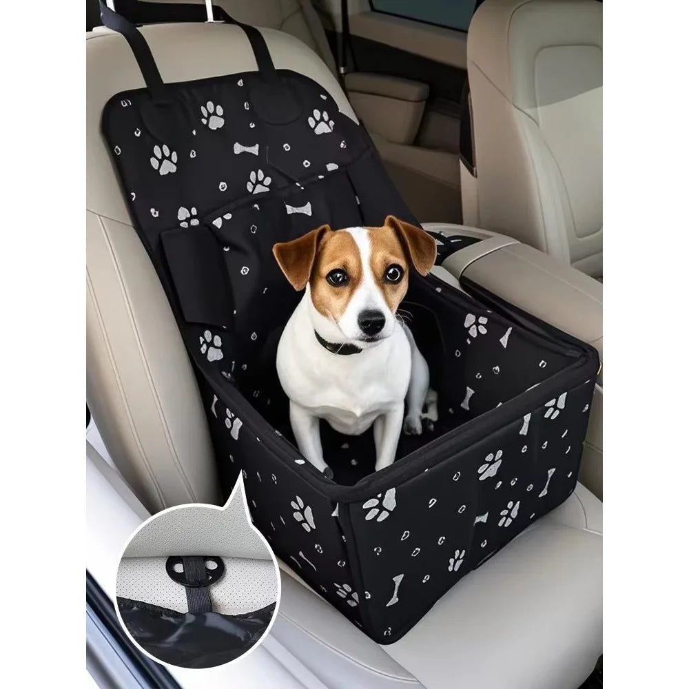 Dog sitting in a black pet car seat cover with paw prints on a car seat.