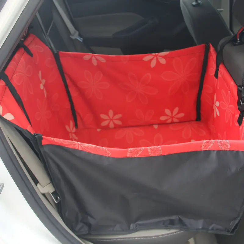 Red and black pet car seat cover with floral pattern inside a vehicle.